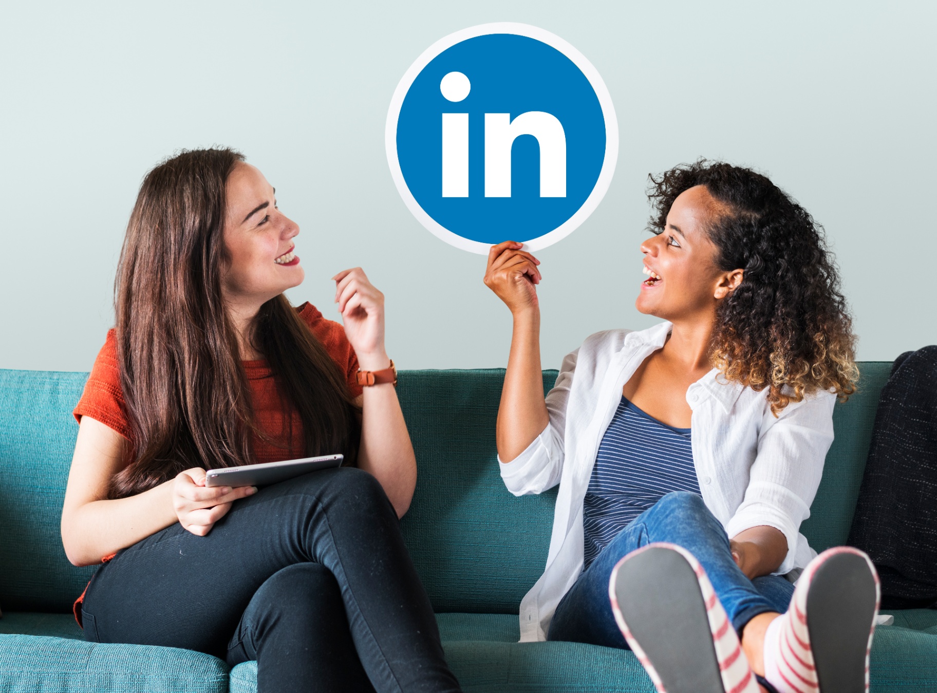 Two women laughing together holding a LinkedIn logo, representing real human B2B conversations.